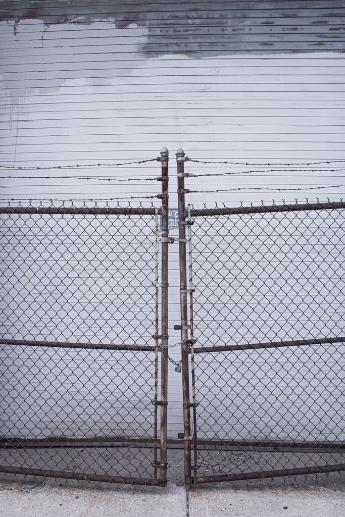 A rusty chain-link fence topped with barbed wire against a metal shutter background.