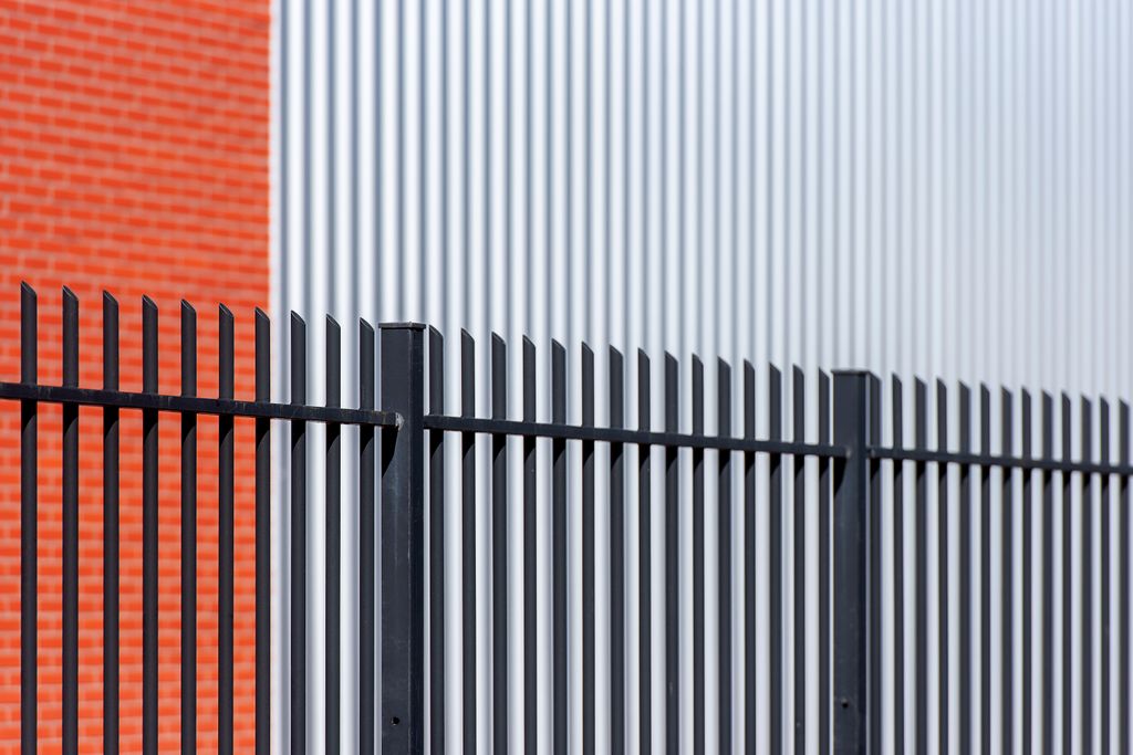 Black metal fence contrasts with red brick and corrugated metal backdrop, offering a sleek industrial look.