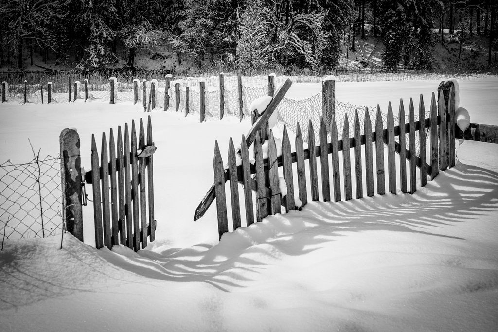 Snowy rural scene in Krün, Germany featuring a rustic wooden fence and open gate.