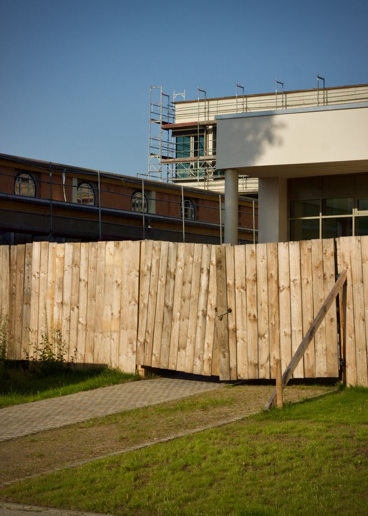 View of a construction site with wooden fence, scaffolding, and modern building structure.